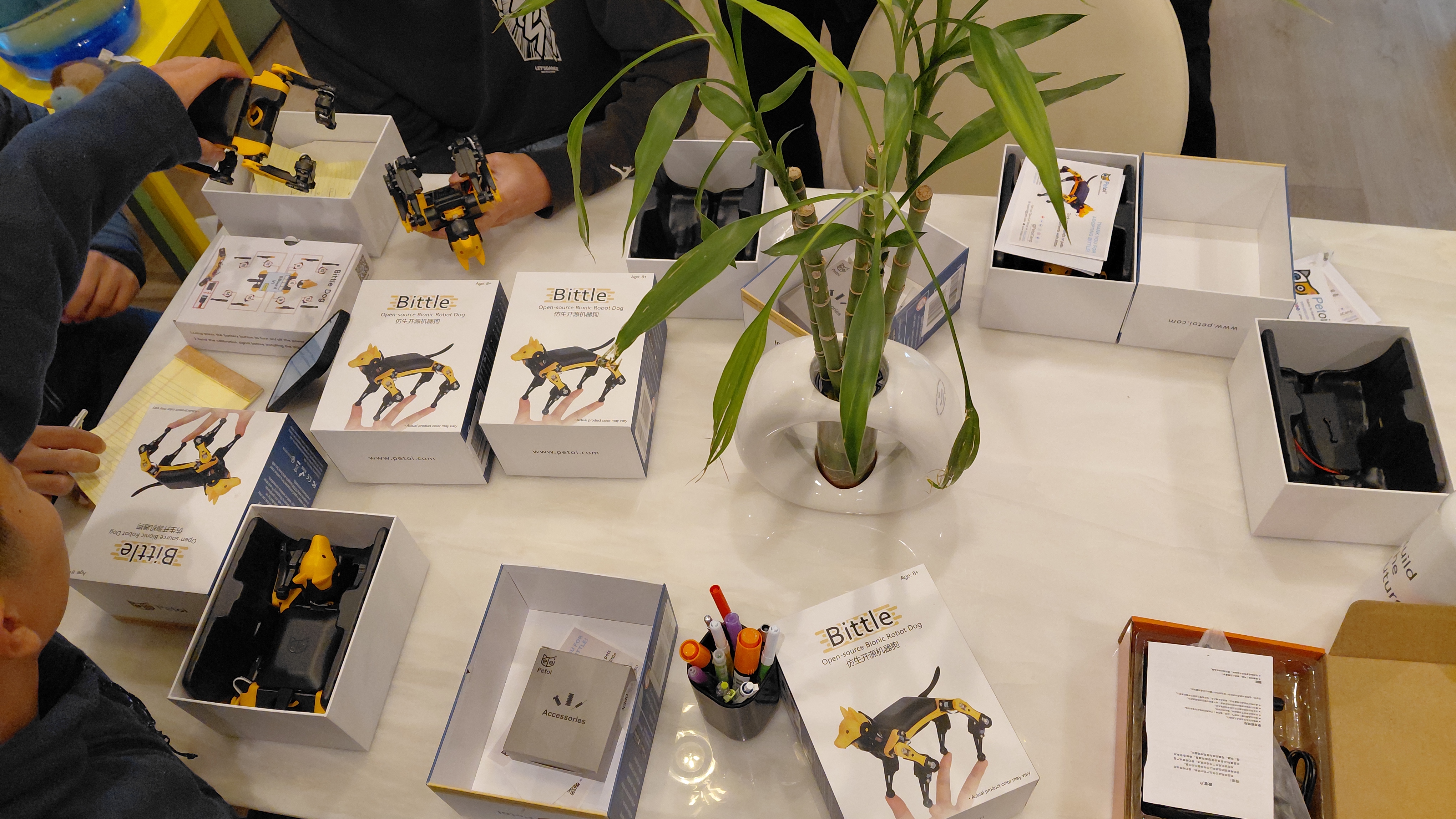 Workshop table with Petoi Bittle robot kits, boxes, and participants assembling yellow and black robots