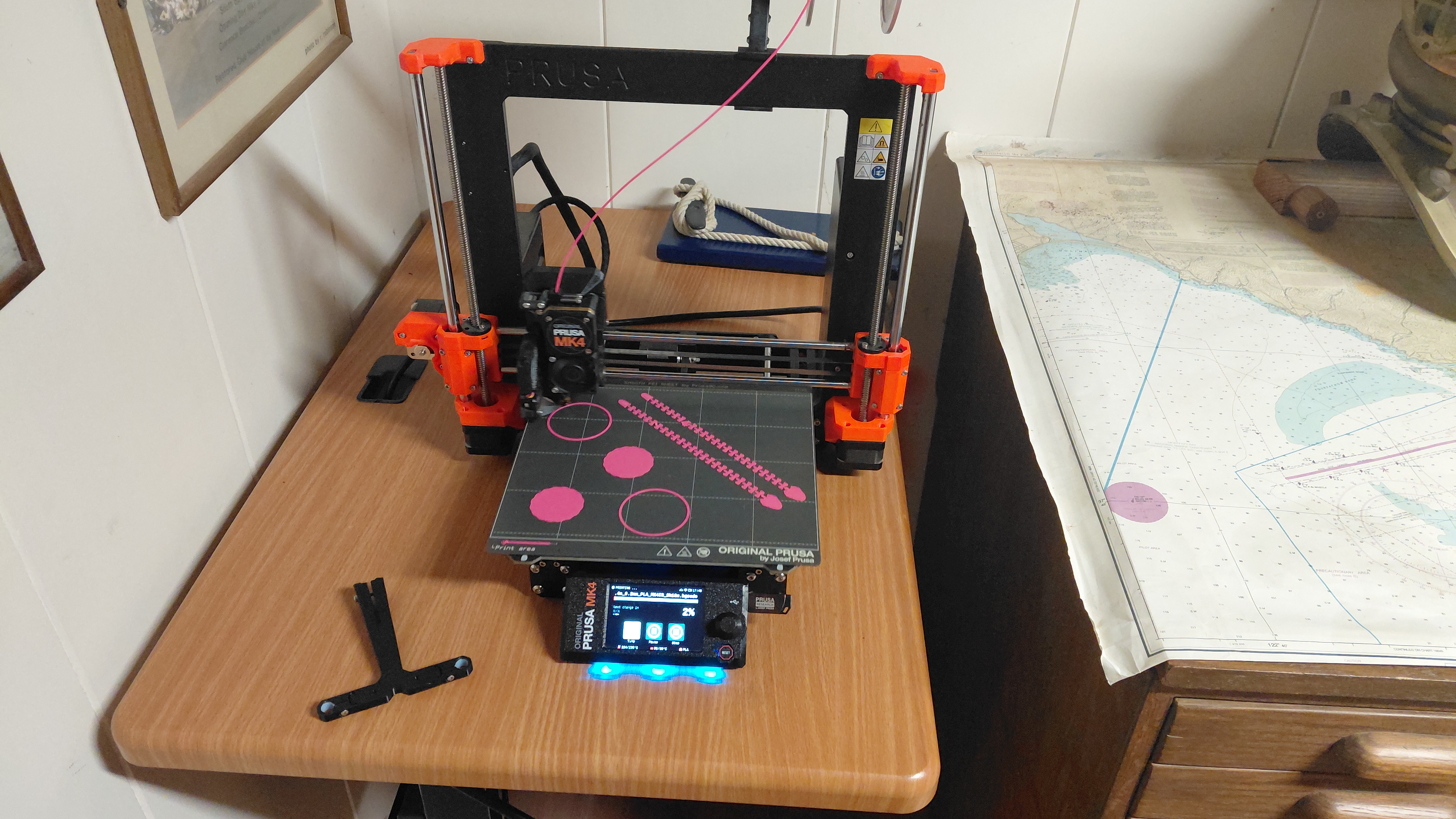 Prusa MK4 3D printer actively printing pink parts on a wooden desk
